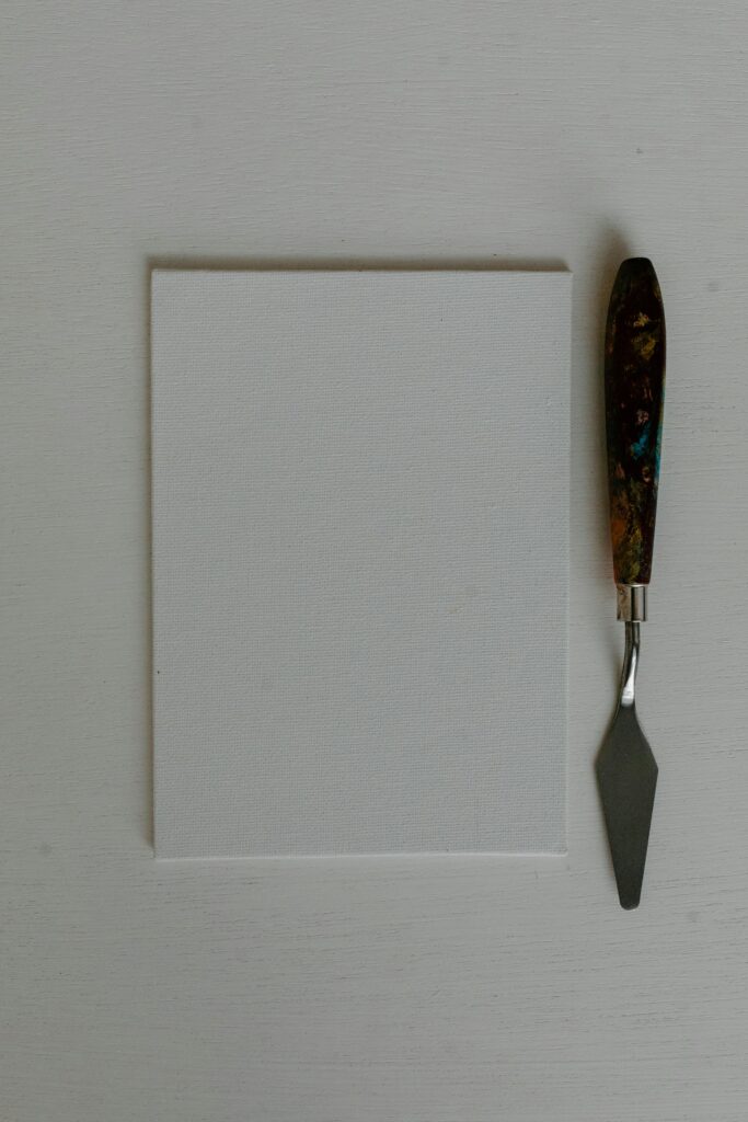 Vertical shot of a blank canvas and palette knife on a table, ideal for art projects.